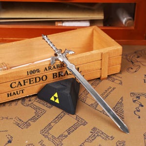 Close-up view of the Legend of Zelda Master Sword Letter Opener highlighting the detailed Triforce engraving, metallic shine, and durable construction. Perfect for gaming room decor, geek office accessories, and fantasy-themed holiday decorations. An excellent Zelda-themed gift idea for men, women, or teens who love video games, making it one of the best-selling Christmas gamer gifts and unique collectible sword items on the Etsy platform.