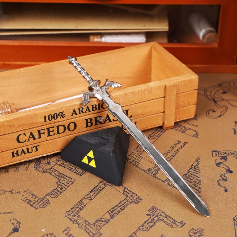 Close-up view of the Legend of Zelda Master Sword Letter Opener highlighting the detailed Triforce engraving, metallic shine, and durable construction. Perfect for gaming room decor, geek office accessories, and fantasy-themed holiday decorations. An excellent Zelda-themed gift idea for men, women, or teens who love video games, making it one of the best-selling Christmas gamer gifts and unique collectible sword items on the Etsy platform.