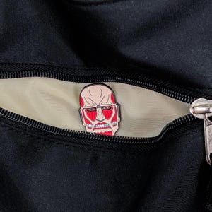 Colossal Titan enamel pin placed on a denim jacket lapel to demonstrate its wearable size and pop culture fashion appeal. The red and black titan design contrasts with the blue fabric, showcasing its striking appearance. The pin’s secure rubber clutch is not visible from this angle, giving it a seamless accessory look. This product image is targeted at anime fans who enjoy customizing streetwear and accessories with themed merchandise and collectible items.