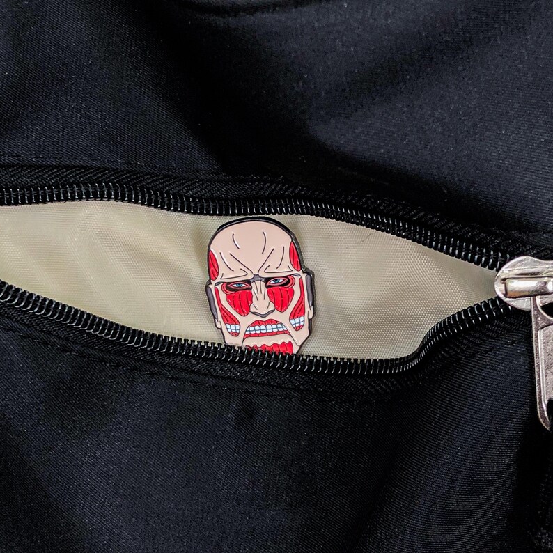 Colossal Titan enamel pin placed on a denim jacket lapel to demonstrate its wearable size and pop culture fashion appeal. The red and black titan design contrasts with the blue fabric, showcasing its striking appearance. The pin’s secure rubber clutch is not visible from this angle, giving it a seamless accessory look. This product image is targeted at anime fans who enjoy customizing streetwear and accessories with themed merchandise and collectible items.