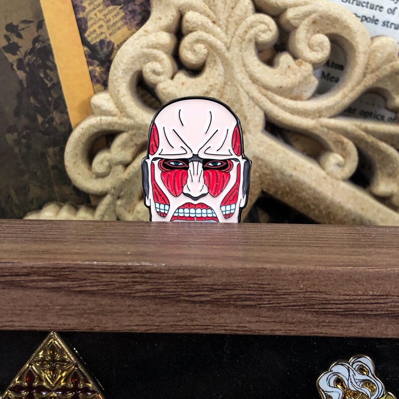 Colossal Titan enamel pin placed on a denim jacket lapel to demonstrate its wearable size and pop culture fashion appeal. The red and black titan design contrasts with the blue fabric, showcasing its striking appearance. The pin’s secure rubber clutch is not visible from this angle, giving it a seamless accessory look. This product image is targeted at anime fans who enjoy customizing streetwear and accessories with themed merchandise and collectible items.
