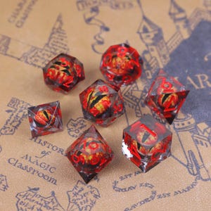 May include: Set of seven polyhedral dice with a red and yellow eye design encased in clear resin. The dice have red numbers and are designed for tabletop role-playing games.