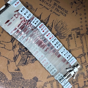 May include: A deck of playing cards with a bloody design. The cards are arranged in order from Ace to King. The cards are on a brown surface with a map of Hogwarts.