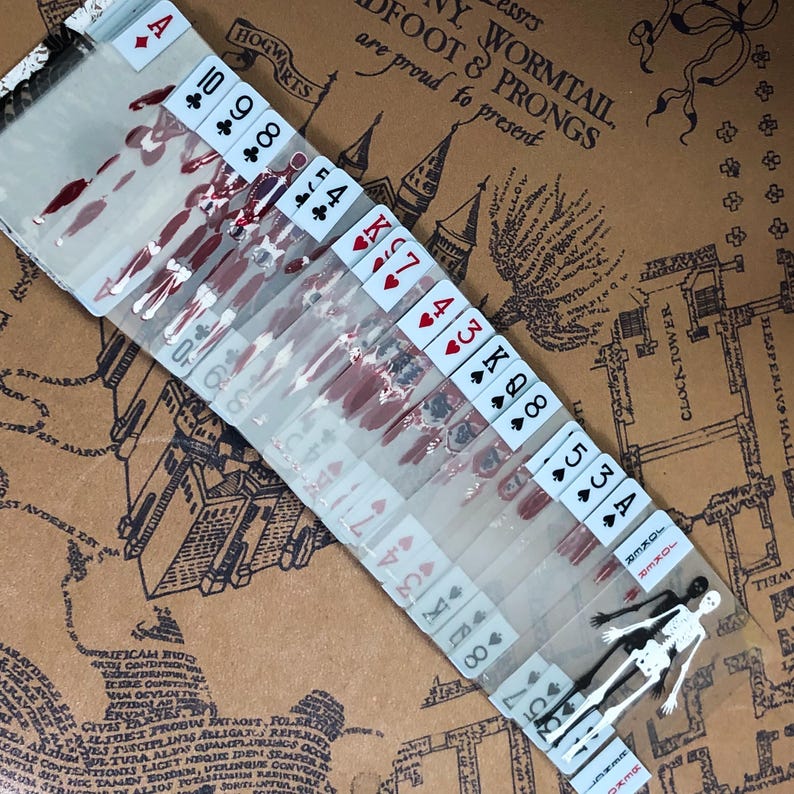 May include: A deck of playing cards with a bloody design. The cards are arranged in order from Ace to King. The cards are on a brown surface with a map of Hogwarts.