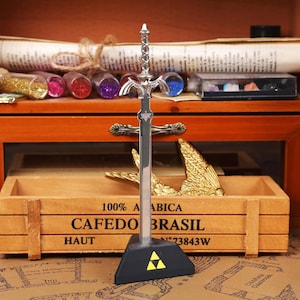 Zelda Master Sword Letter Opener with Triforce stand displayed on a gamer’s desk, showcasing its premium metal build and intricate hilt design, perfect for Zelda fans, TOTK and BOTW collectors, and fantasy lovers looking for a functional and decorative desk accessory. This high-quality zinc alloy sword replica doubles as a collectible display and practical envelope opener, making it ideal for Christmas gamer gifts, stocking stuffers, Halloween decorations, and unique holiday season gifts on Etsy