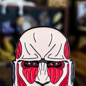 Colossal Titan enamel pin featuring intense red muscle detailing and bold black outline, inspired by the iconic character from Attack on Titan anime. The pin is shown up close to highlight the vivid color contrast and fine craftsmanship of the zinc alloy with soft enamel finish. Ideal for anime fans, cosplayers, and collectors, the pin is designed to be worn on jackets, bags, or displayed with other fandom collectibles. Photographed on a neutral background to showcase design clarity.