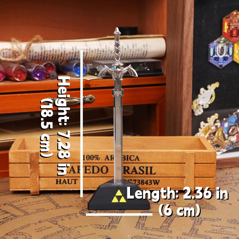 May include: A silver-colored decorative sword, 7.28 inches (18.5 cm) tall, with a black base and a yellow triangle emblem. The sword's length is 2.36 inches (6 cm). The background includes a wooden box and various decorative items.