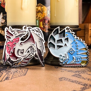 May include: Two metal dragon-themed keychains. One keychain features a red, white, and black dragon design. The other keychain has a blue, white, and black dragon design. Both keychains have a silver-coloured border and a small loop for attaching to a keychain.