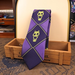 May include: A purple necktie with a repeating diamond pattern. Each diamond features a yellow skull design. The tie is made of a smooth fabric and is displayed on a wooden box.