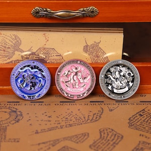 May include: Three round metal coins with intricate designs. One is blue with a sea creature, another is pink with "Chemistry" text, and the third is gray with "Physics" text. Each coin has Latin text around the edge.