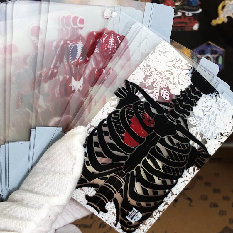 Close-up image of a single Transparent Skeleton Slice Playing Card held between fingers under natural light, highlighting the clarity of the transparent PVC material and the crisp anatomical skeleton illustration in red UV ink, perfect for illusionists, students, and those who appreciate unique poker deck aesthetics.