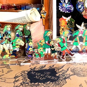 May include: A set of 12 colorful cartoon character acrylic charms featuring a green, white, and brown color scheme. The characters are standing on a clear acrylic base.