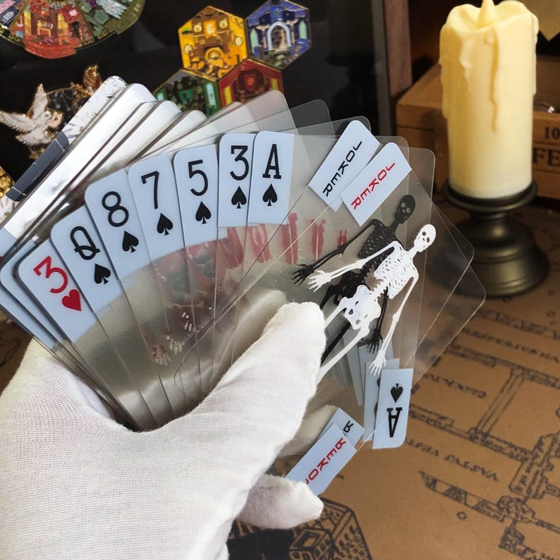 Close-up image of a single Transparent Skeleton Slice Playing Card held between fingers under natural light, highlighting the clarity of the transparent PVC material and the crisp anatomical skeleton illustration in red UV ink, perfect for illusionists, students, and those who appreciate unique poker deck aesthetics.