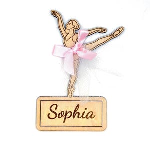 May include: Wooden ballerina figure with a pink bow and the name "Sophia" engraved on a rectangular base. The ballerina is in a graceful pose, with one leg extended and arms raised. The figure is made of light-colored wood.