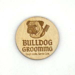 May include: A round, wooden sign with the words "BULLDOG GROOMING" in a bold font, and the tagline "Tough Looks, Gentle Care." A detailed engraving of a bulldog's head and a comb is above the text. The sign is made of light-colored wood.
