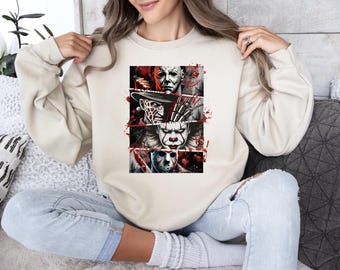 May include: Beige sweatshirt featuring a graphic of horror movie villains, including Michael Myers, Freddy Krueger, Pennywise, and Jason Voorhees. The design has a red splatter effect. The sweatshirt is a neutral color.
