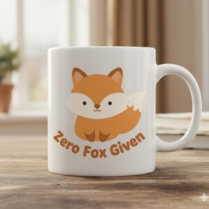 May include: White ceramic mug featuring a cartoon fox in shades of orange and white. The mug has the text "Zero Fox Given" in brown. The mug has a curved handle and is set on a wooden surface.