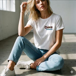 May include: White crew neck t-shirt with the text "Chaos Coordinator" in a distressed font. The shirt is paired with light blue jeans and white sneakers. The person is sitting on a concrete floor.