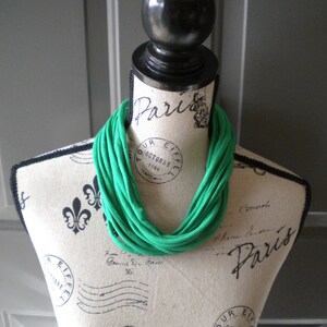May include: A green fabric necklace on a white mannequin with black trim and a Paris design. The necklace is made of multiple loops of fabric.