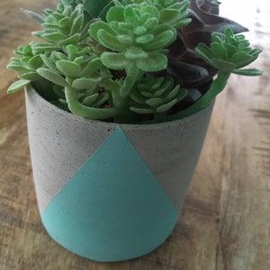 May include: A small concrete planter with a light blue geometric design, filled with a variety of green succulents.