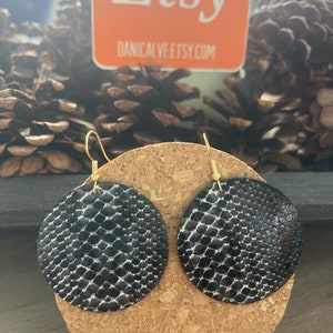 May include: A pair of round, black and white snake print earrings with gold-colored hooks. The earrings are displayed on a cork surface. The Etsy logo is visible in the background.