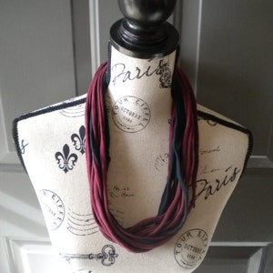 May include: A burgundy and black infinity scarf made of fabric. The scarf is displayed on a mannequin with a Parisian theme.