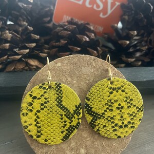 May include: A pair of yellow and black snake skin patterned earrings. The earrings are round and have a gold hook.