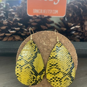 May include: A pair of yellow and black teardrop-shaped earrings with a snake skin pattern. The earrings are made of leather and have gold hooks.