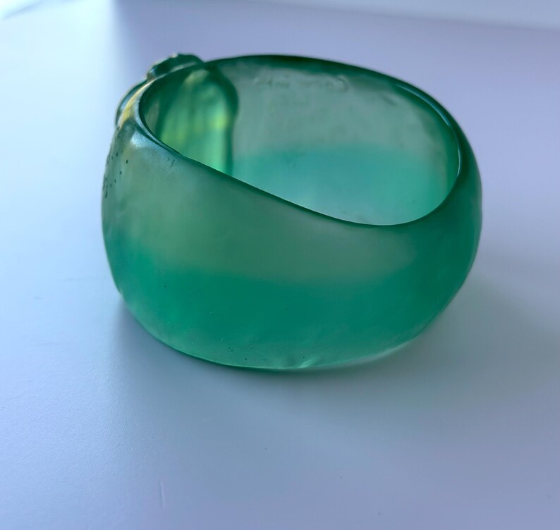May include: A translucent, rounded, teal-coloured glass bowl. The bowl has a smooth, glossy exterior and a slightly textured interior. The bowl's shape is organic, with a wide opening and a curved base. The glass appears to be hand-blown.