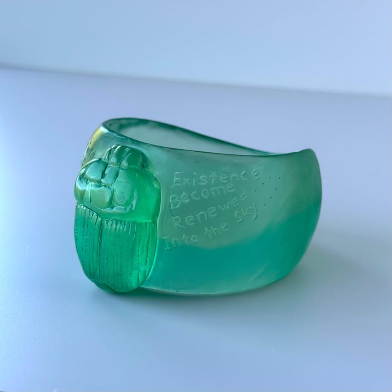 May include: A translucent green glass bowl with a scarab beetle design. The bowl has the words "Existence Become Renewed Into the Sky" etched into the side.