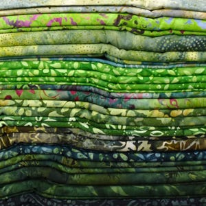 May include: A stack of folded fabric in various shades of green, with floral and abstract patterns. The fabrics range from light to dark green, with accents of pink, purple, and blue. The textiles appear to be cotton or a similar material, suitable for quilting or crafting.