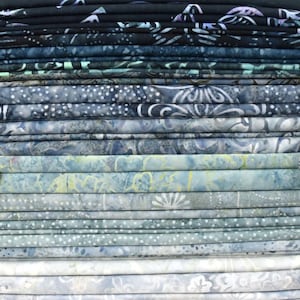 May include: A stack of folded fabric in shades of blue, teal, and gray. The fabric has various patterns, including floral and dotted designs. The fabrics are neatly stacked, showcasing a gradient of colors from dark to light.