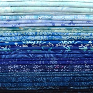 May include: A stack of folded fabric in various shades of blue, ranging from light sky blue to deep navy. The fabrics feature a variety of patterns, including floral, swirls, and abstract designs. The image showcases a gradient of blues.