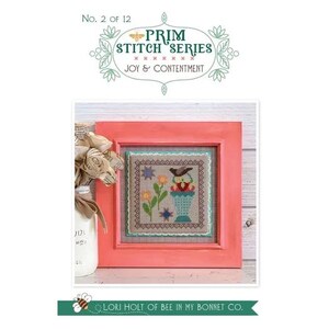 May include: A framed cross-stitch sampler with a floral and bird design. The sampler is in a coral-colored frame and features the text "PRIM STITCH SERIES JOY & CONTENTMENT". A vase of paper flowers sits to the left.