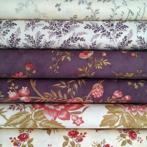 May include: A stack of fabric rolls featuring various floral and botanical patterns. The fabrics display a range of colors, including cream, purple, red, and brown. The designs include detailed floral prints and stylized leaf patterns.