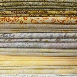 May include: A stack of folded fabric pieces in various shades of yellow, gold, beige, and olive green. The textiles feature diverse patterns including floral motifs, abstract swirls, and subtle geometric designs with a batik-style appearance.