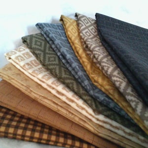 May include: A stack of folded fabric squares featuring various patterns including brown and black gingham, tan grid, cream with geometric shapes, olive green diamond, blue gray diamond, mustard yellow, tan chevron, and a dark charcoal gray fabric.