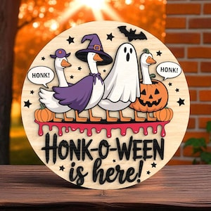 May include: Wooden round sign with a Halloween theme. Features cartoon geese dressed in costumes, including a witch, ghost, and jack-o'-lantern. The sign reads "Honk-o-ween is here!" with star and bat accents.