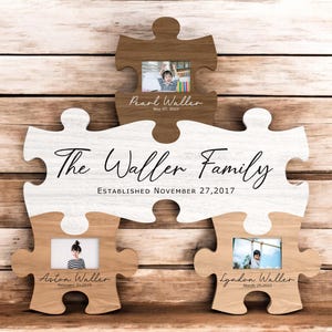 Puede incluir: Un expositor de fotos familiar de madera con forma de piezas de rompecabezas. La pieza superior tiene una foto y el nombre "Pearl Waller" con la fecha "May 07, 2003". La pieza central dice "The Waller Family" y "ESTABLISHED NOVEMBER 27,2017".