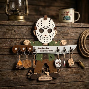 May include: Wooden Camp Crystal Lake key holder featuring a character with a hockey mask holding a knife with key hooks. Includes keychains with a campfire, camp supplies box, and a flashlight. The text "Kee-kee-kee... Maa-maa-maa..." is on the knife.