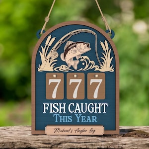 May include: Wooden fishing-themed sign with a blue background and brown frame. The sign features a fish, fishing rod, and the number 777. Text reads "FISH CAUGHT THIS YEAR" and "Michael's Angler Log."