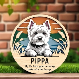 Peut inclure: Panneau rond en bois avec une illustration de chien West Highland Terrier blanc. Le panneau comprend le nom "Pippa" et le texte "By the lake, your memory rests with the breeze." Le fond représente une scène de lac.