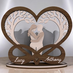 May include: A wooden heart-shaped sculpture with a tree design and a couple embracing. The sculpture has a dark brown frame with a light-colored interior. The names "Lucy" and "Anthony" are inscribed on the base. A unique wedding or anniversary gift.