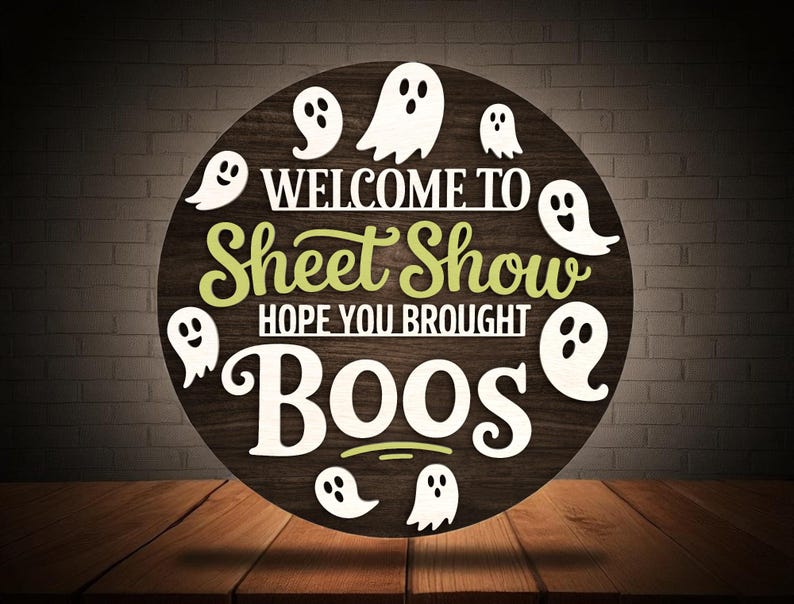 Puede incluir: Cartel de madera redondo con el texto "WELCOME TO Sheet Show HOPE YOU BROUGHT BOOS" en letras blancas y verdes. Figuras de fantasmas blancos salpican el cartel, que se encuentra sobre un fondo de madera oscura.
