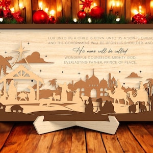 Peut inclure: Une scène de nativité de Noël en bois avec un cadre marron. La scène représente une étoile, des palmiers et des silhouettes de personnes et d'animaux. Le texte comprend "For unto us a child is born..." et "His name will be called..."