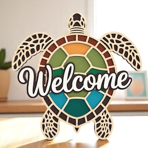 May include: Wooden turtle-shaped sign with the word "Welcome" in white script. The turtle's shell features a mosaic design with shades of green, orange, and blue. The sign is made of layered wood and has a natural wood finish.