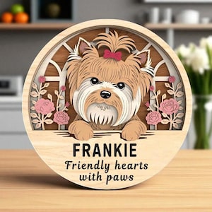 May include: A wooden, layered dog portrait featuring a Yorkshire Terrier with a pink bow. The dog is framed by a window design with pink roses. The name "FRANKIE" and the phrase "Friendly hearts with paws" are below.