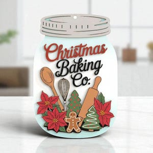 May include: A mason jar-shaped sign for Christmas Baking Co. with a wooden spoon, whisk, rolling pin, gingerbread man, and Christmas tree. Red poinsettias and the text "Christmas Baking Co." are also included.