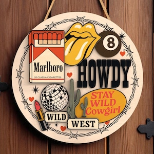 Peut inclure: Panneau rond en bois sur le thème du Far West. Il présente un paquet de cigarettes Marlboro, une boule disco, un cactus et les mots "HOWDY" et "STAY WILD Cowgirl". Orné de cœurs et de fil de fer barbelé.