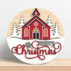Puede incluir: Decoraci&oacute;n navide&ntilde;a redonda de madera con una iglesia roja, tejado negro y nieve blanca. Las palabras "merry Christmas" est&aacute;n escritas en rojo y gris. Los &aacute;rboles blancos flanquean la iglesia.